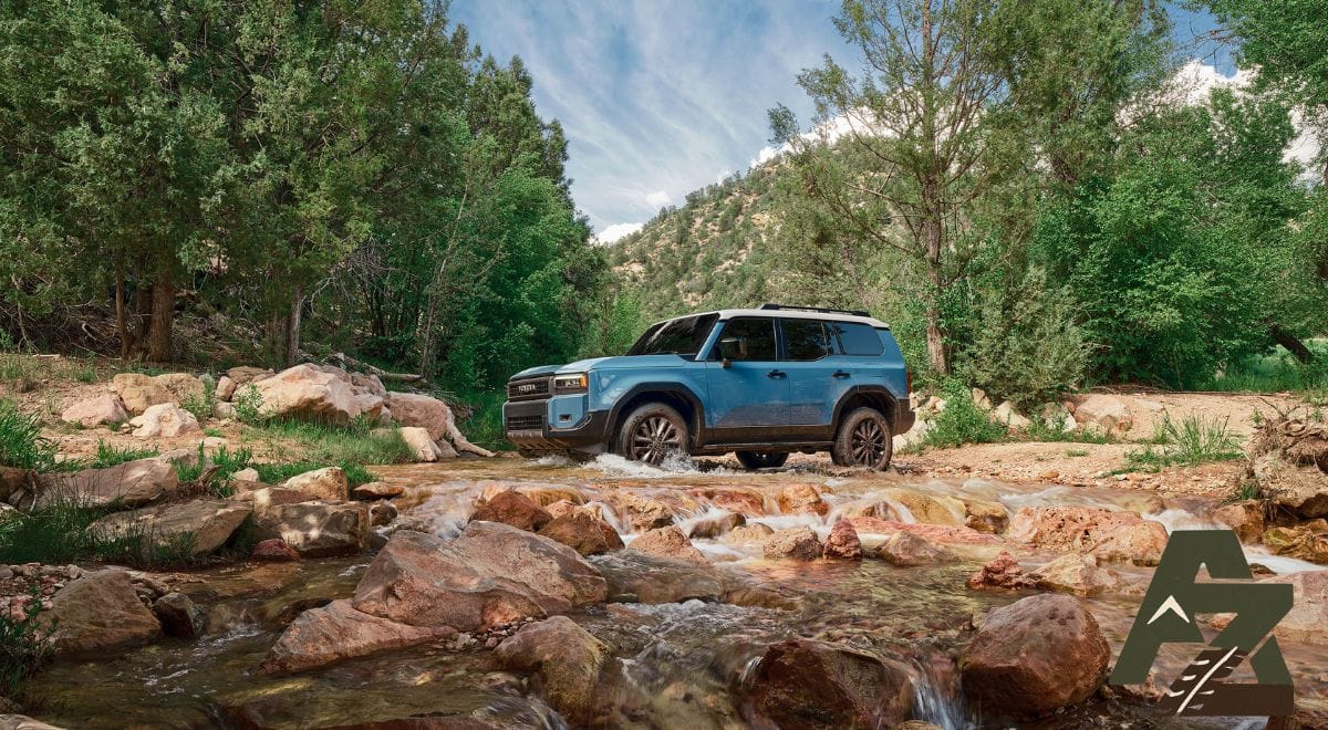 2025 Toyota Land Cruiser J250 driving off-road in Heritage Blue, showcasing retro design and rugged stance.